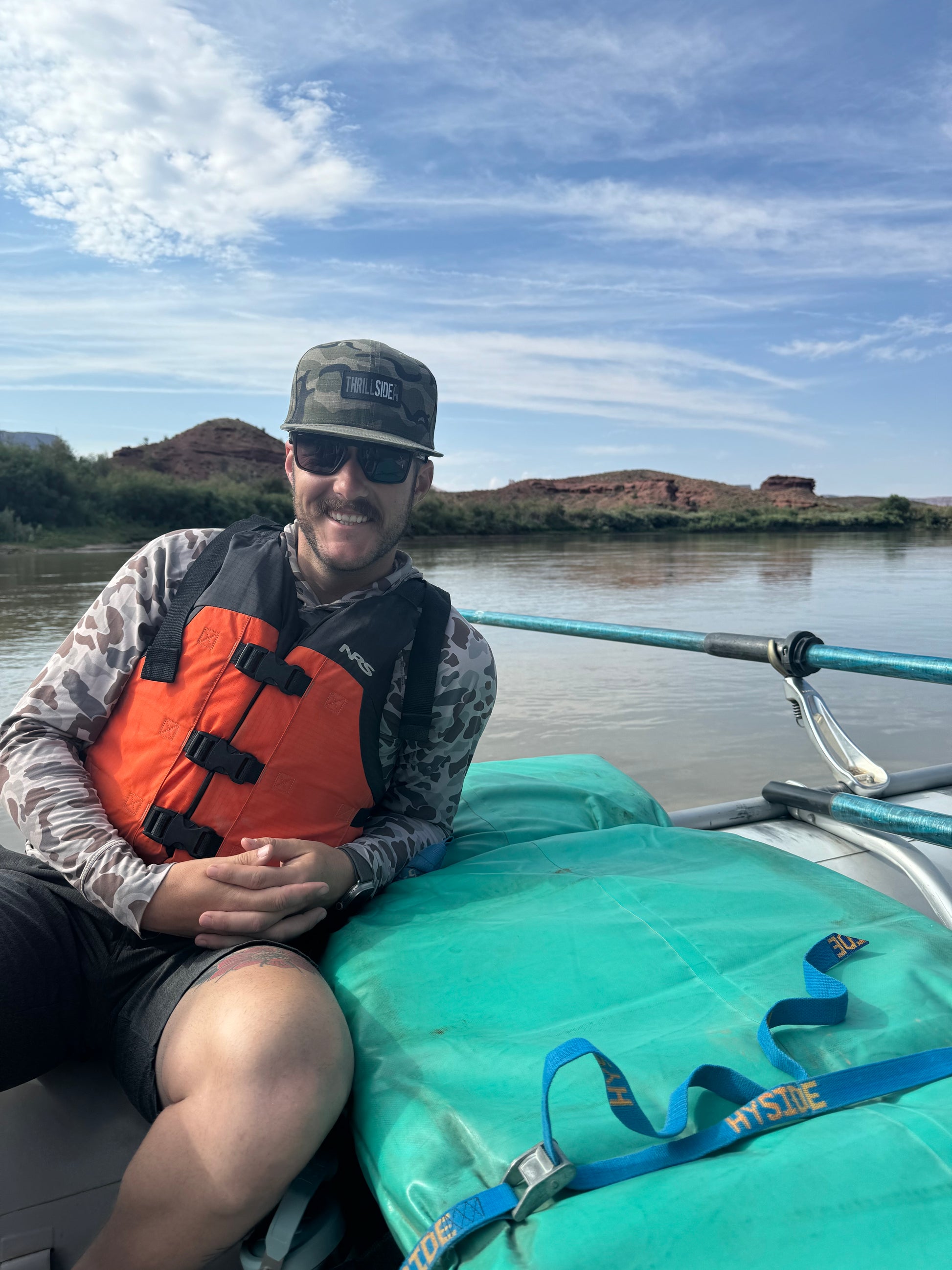 Whitewater rafter wearing a West Desert light multicam hat and personal floatation device
